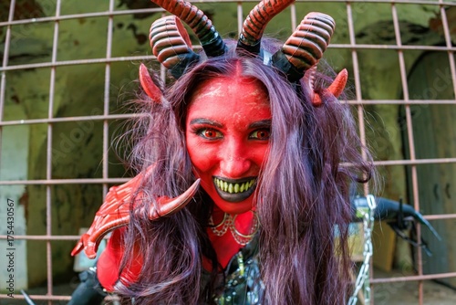 Demonic cosplay woman with horns and chains behind metal bars