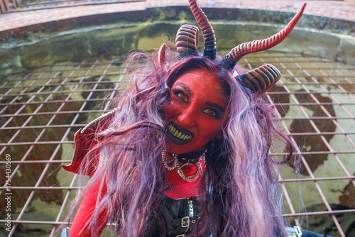 Demonic cosplay woman with horns and chains behind metal bars