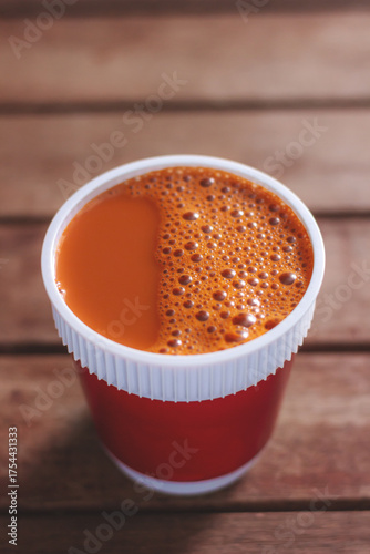 Hot milk tea in a red cup on wooden table blurred background