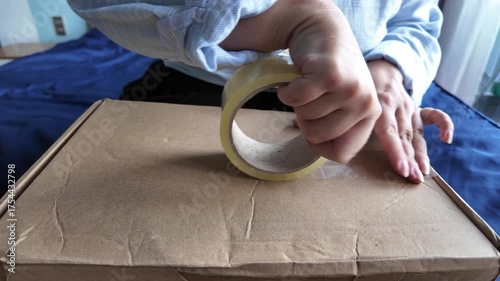 Close-up of a woman's hands taping a cardboard box with adhesive tape, front view