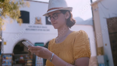 Young Woman in Hat Using Smartphone on Cozy European Street While Texting with Friends