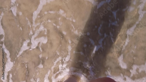 Women's feet walking barefoot on the beach, water splashing on their feet