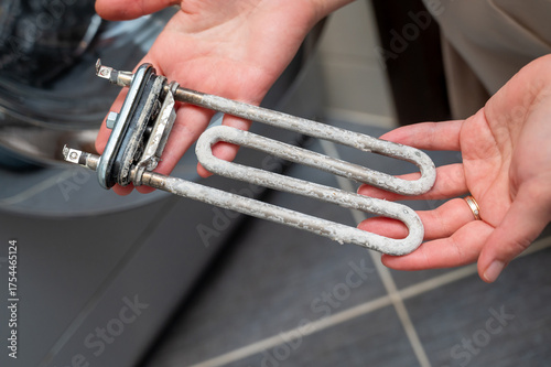 Hands holding washing machine heating element covered with limescale during appliance repair