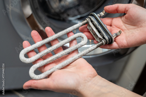 Hands holding washing machine heating element covered with limescale during appliance repair
