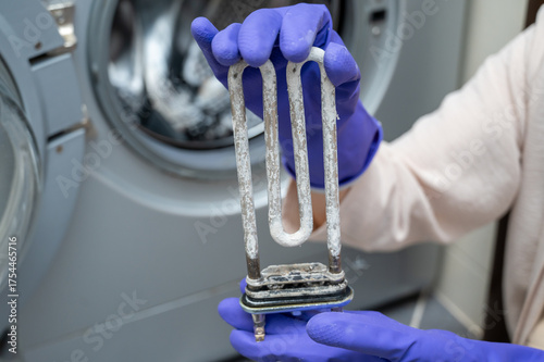 Person in gloves showing removed washing machine heating element covered with limescale