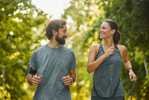 Slika na platnu Two individuals jog side by side in a vibrant park, surrounded by greenery