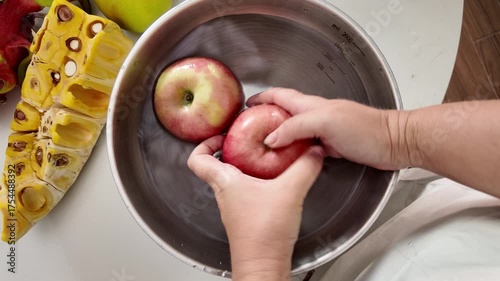 Close-up of a woman's hands in an apron, standing in front of a table with fruit and washing apples