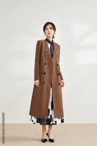 Elegant woman in a brown coat with a patterned dress standing indoors.
