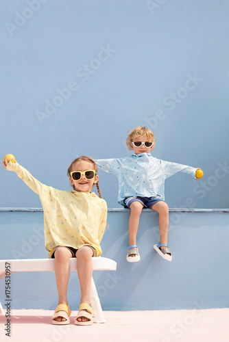 Two children wearing colorful shirts and sunglasses, playing outdoors with joy.