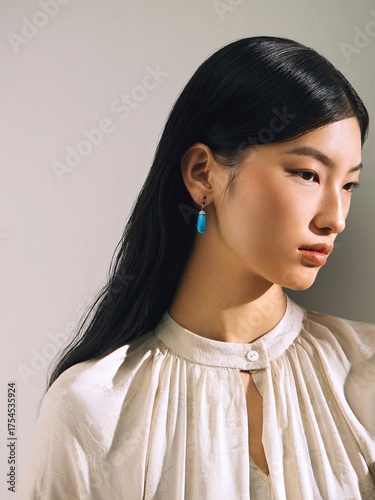 Woman in a soft white blouse with turquoise earrings, posed in a portrait framing, conveying a modern and clean aesthetic.