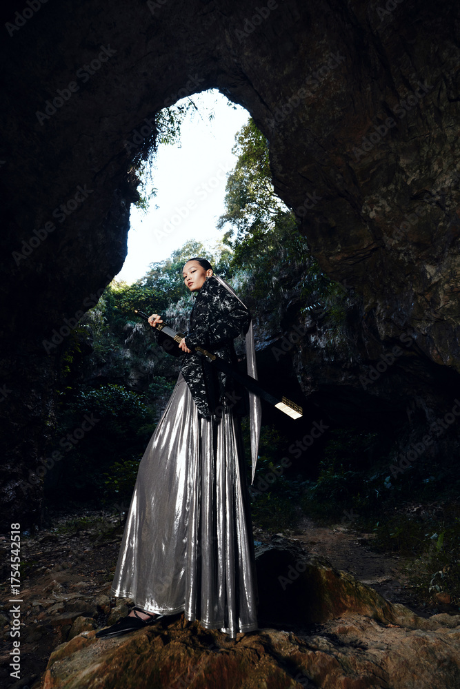 Φωτογραφία Chivalrous Woman in a black and silver long dress holding a sword in a cave setting