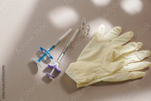 flat lay of various syringes, ampoules, medical gloves, disposable cap arranged on a light background, natural sunlight. Concept of medical preparation or cosmetic procedure setup