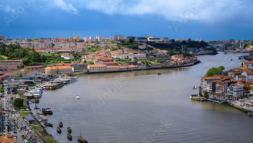 A wide, panoramic, high-angle view of the Douro River flowing through the cities of Porto and Vila Nova de Gaia in Portugal.