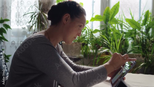 Woman drawing peacock feather on tablet screen while sitting at table in room