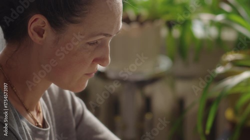 Close-up, woman drawing on tablet screen while sitting at table on the background of houseplants