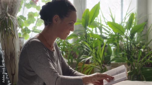 Woman turning a page of a book while reading sitting in a room at a table