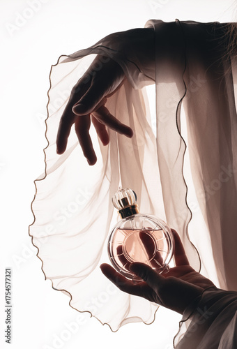A woman's hand elegantly holds a glass perfume bottle on a pink background