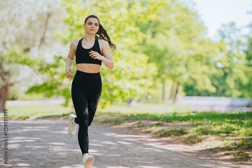 Foto Woman jogging on a sun-dappled path, symbolizing vitality and joy amid verdant park scenery, with momentum and energy in every stride