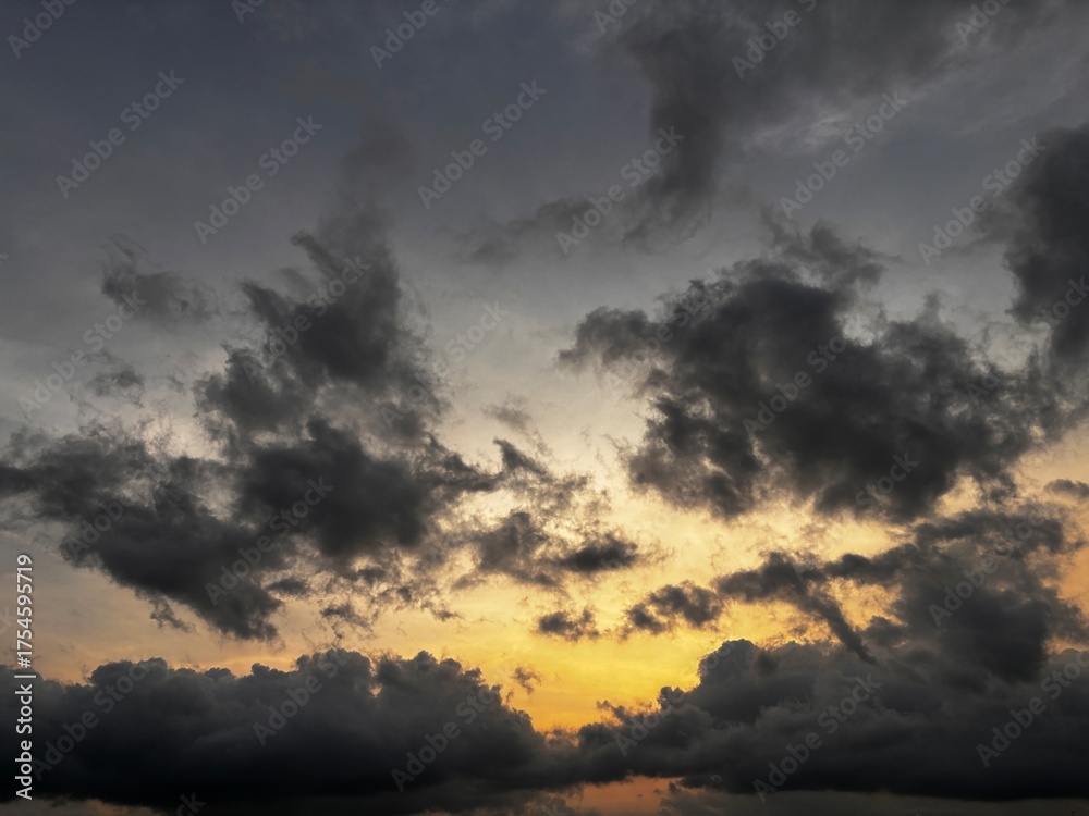 Obraz premium Dramatic sunset sky with dark storm clouds and a warm orange glow on the horizon, creating a powerful contrast between light and shadow in the evening atmosphere.
