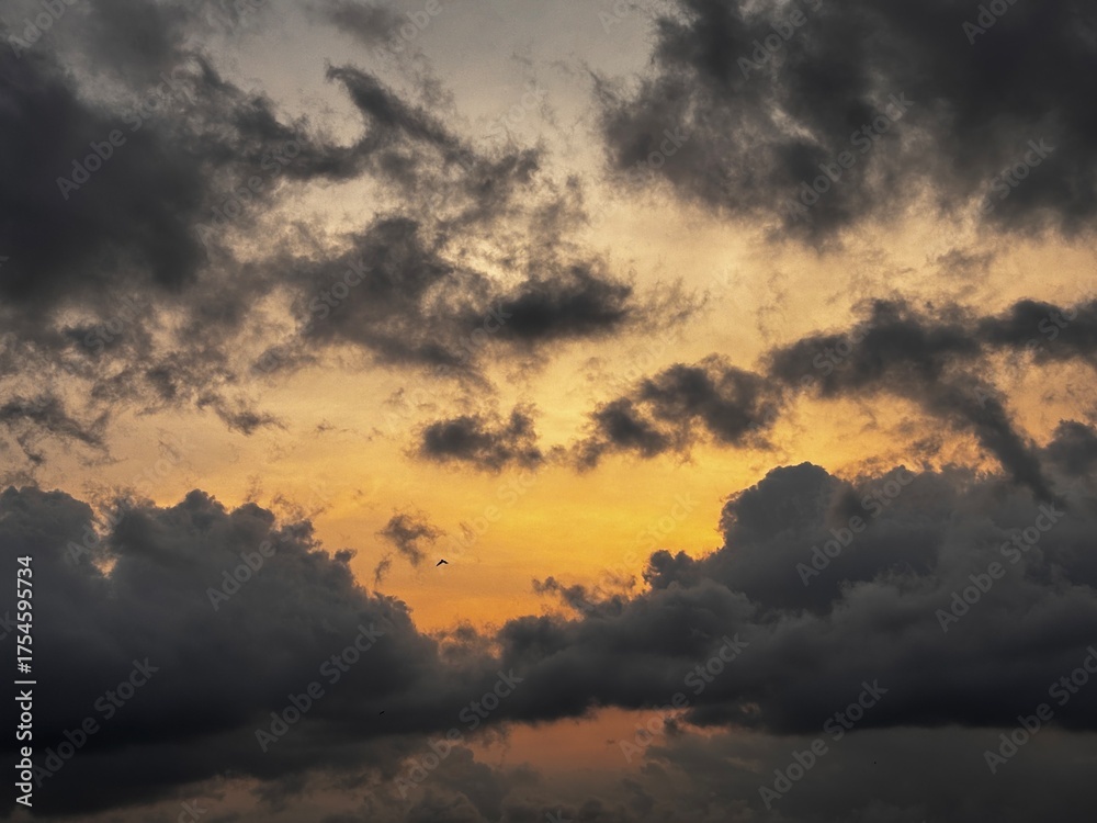 Fototapeta premium Dramatic sunset sky with dark storm clouds and a warm orange glow on the horizon, creating a powerful contrast between light and shadow in the evening atmosphere.