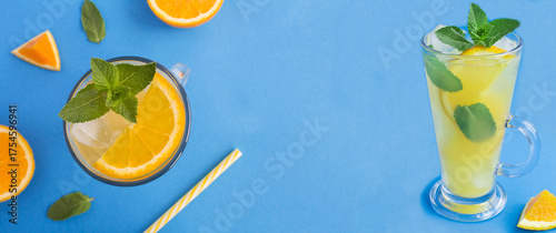 Cold lemonade or infused water with orange, mint and ice cube in the drinking glass on a blue background. Copy space.