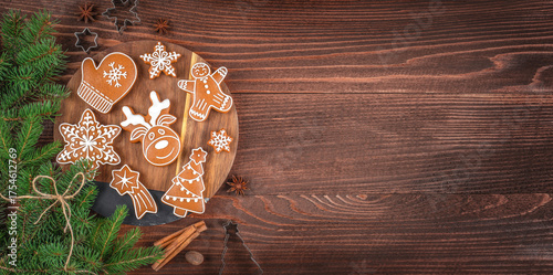 Christmas holiday concept with decorated gingerbread cookies on a wooden board, fir branches, spices, and empty copy space for festive greetings, bakery advertising, or winter recipe design
