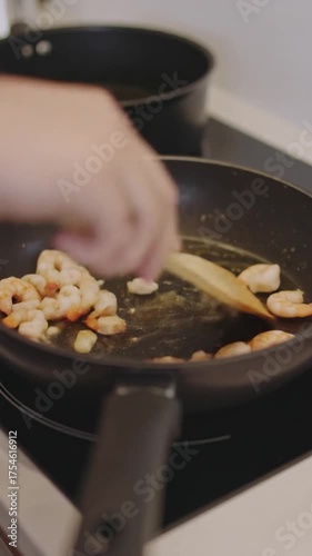Person cooking shrimp and garlic in a hot frying pan on a modern stovetop, stirring with a wooden spoon