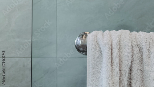 Clean white towel hanging on metal bar in a modern bathroom with tile wall, minimal design and hygiene lifestyle concept, spa or hotel interior.