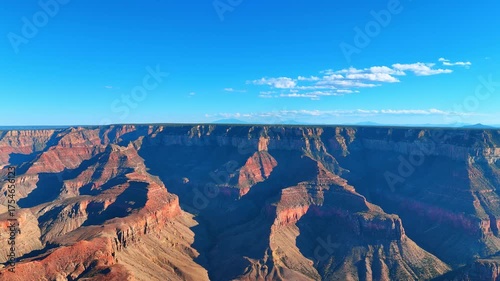 Amazing canyons dazzled with bright sun. Few white fluffy clouds in the blue sky above. The Grand Canyon National Park, Arizona, USA. Aerial view.
