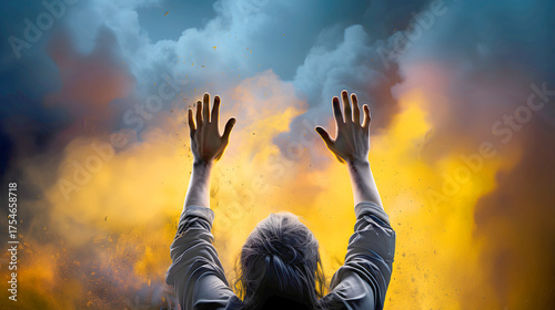 Person raising hands in triumph while standing before a wall of rocks with a flowing fabric in a dramatic sky setting