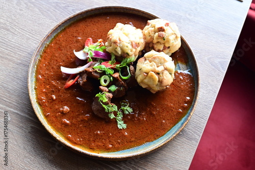 Close-up top view of traditional Czech goulash with Karlovy Vary dumplings, served on a wooden table in a restaurant. The rich colors and textures of the dish highlight the warmth and authenticity