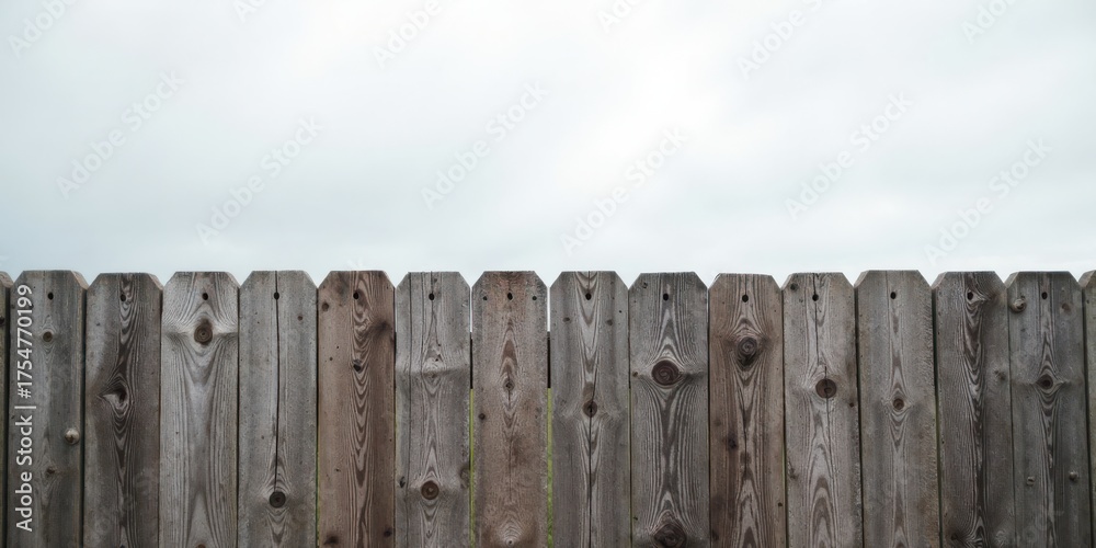 Fototapeta premium A weathered wooden fence stretches across the image, its aged planks showing the passage of time against a pale, overcast sky.