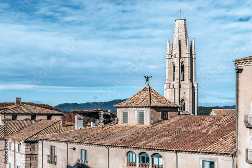 Historic Girona cityscape with Sant Feliu bell tower above terracotta rooftops, showcasing Mediterranean architecture and distant mountains under a clear Catalan sky, Spain