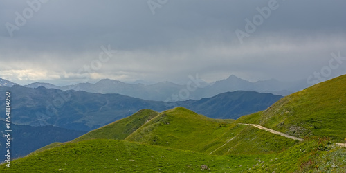  Green meadow with mountain peaks covered in mist and clouds. La Vanoise national park, Savoie, France 