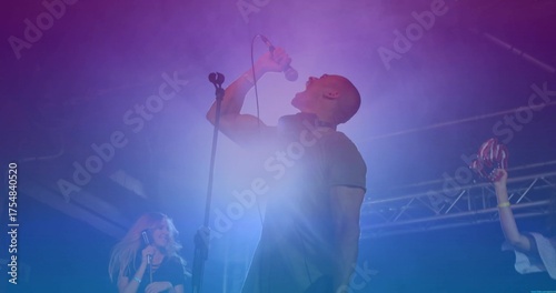 Gripping microphone singer belting out song on stage, with red maracas and colored LED lights