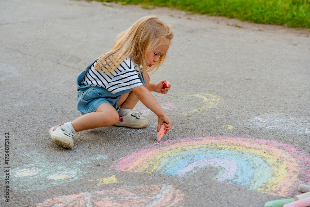 Naklejka premium Cute little girl draws with crayons on asphalt.