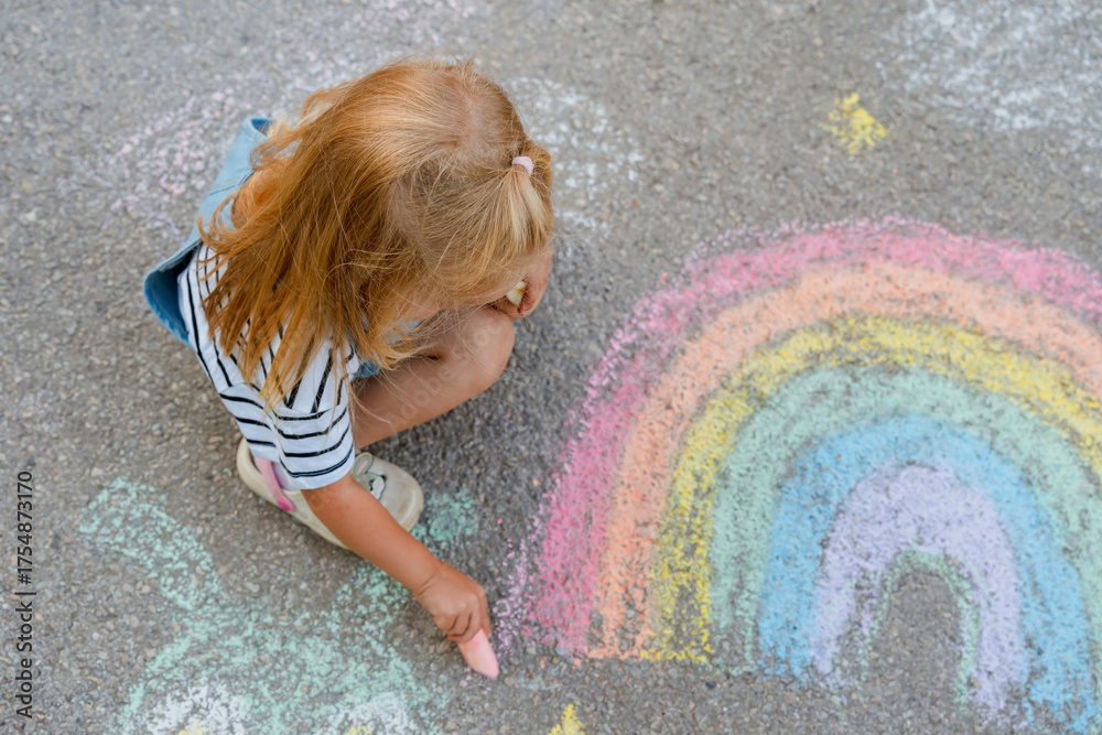 Fototapeta premium Cute little girl draws with crayons on asphalt.