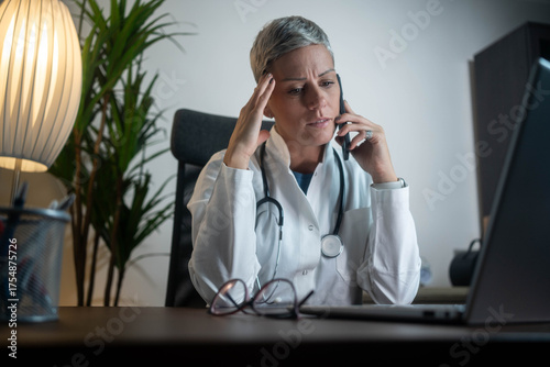 Stressed female doctor making phone call in modern clinic office, concerned about patient results, professional
