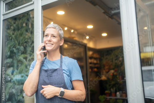 Smiling female florist talking on phone taking flower orders from customers in her small business flower shop