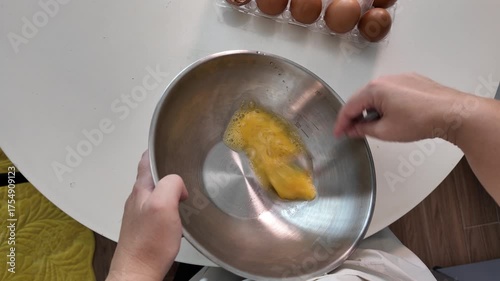Hands of a woman beating eggs in a metal bowl on the kitchen table