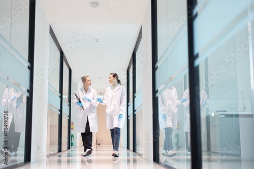 Two researchers walking together in a modern hospital corridor discuss about work