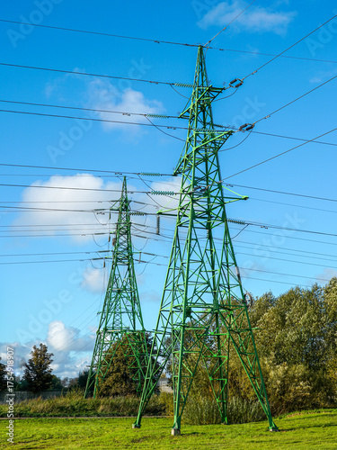 Green electricity pylons with power lines against a bright blue sky in a rural landscape