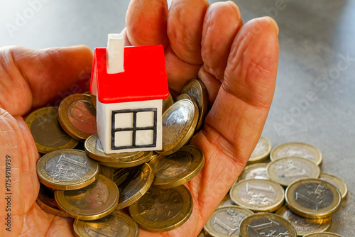 Hand holding euro coins with small red-roof house symbolizing real estate savings and investments