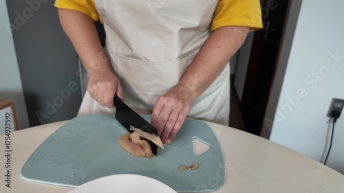 A woman is cooking dinner, slicing chicken fillet on a cutting board.