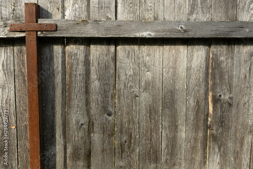 A rustic wooden fence with a cross made of metal. The wood is weathered and shows signs of age. The scene conveys a sense of simplicity and rural life.