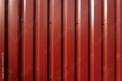 A close-up view of a red corrugated metal wall. The surface features vertical lines and a smooth texture, typical of industrial design.