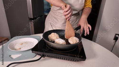 Woman in an apron cooks meatballs. She turns the meatballs over and roasts them in a pan.