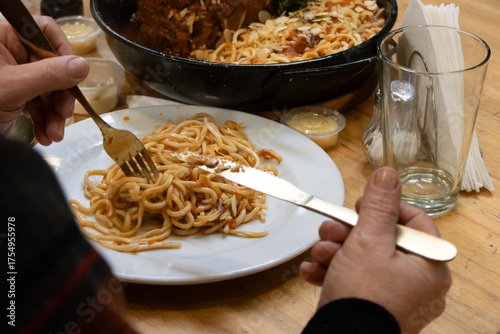 Hands of an adult holding cutlery over a plate of spaghetti with red sauce that she is eating