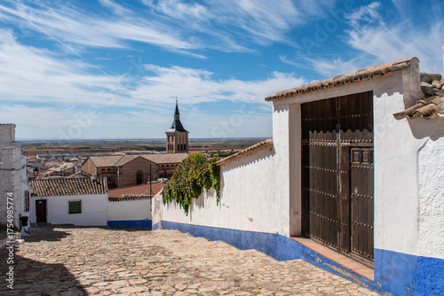 Street with a large wooden gate and white and blue houses and in the background the Church of the Assumption in Campo de Criptana
