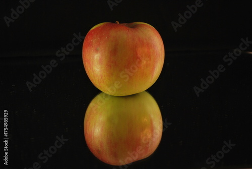 yellow red apple on reflective surface, black background, elegant composition, glossy texture, vivid colors, studio lighting, minimalism